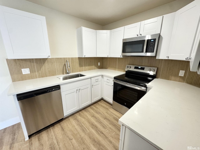 kitchen with appliances with stainless steel finishes, sink, white cabinets, and light wood-type flooring