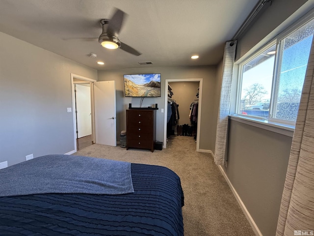 bedroom featuring a walk in closet, light carpet, ceiling fan, and a closet