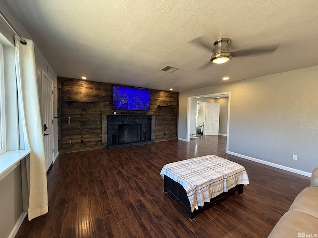 living room featuring ceiling fan, a stone fireplace, dark hardwood / wood-style floors, and a textured ceiling