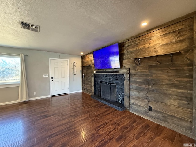 unfurnished living room with dark wood-type flooring, wooden walls, a fireplace, and a textured ceiling