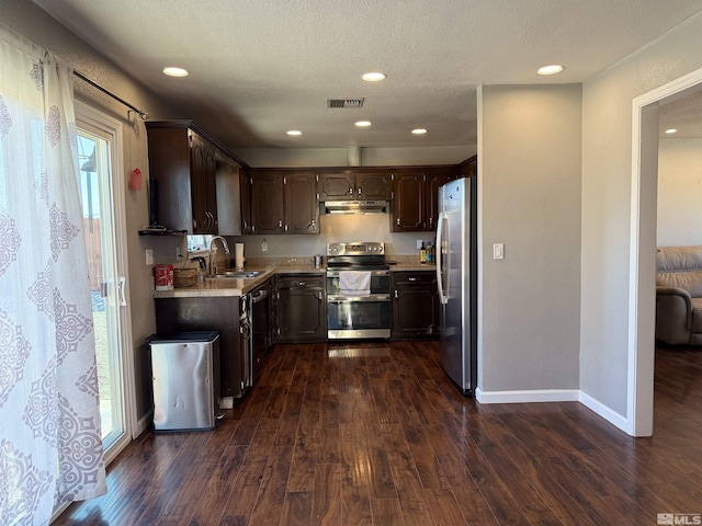 kitchen with appliances with stainless steel finishes, sink, dark brown cabinetry, dark wood-type flooring, and a textured ceiling