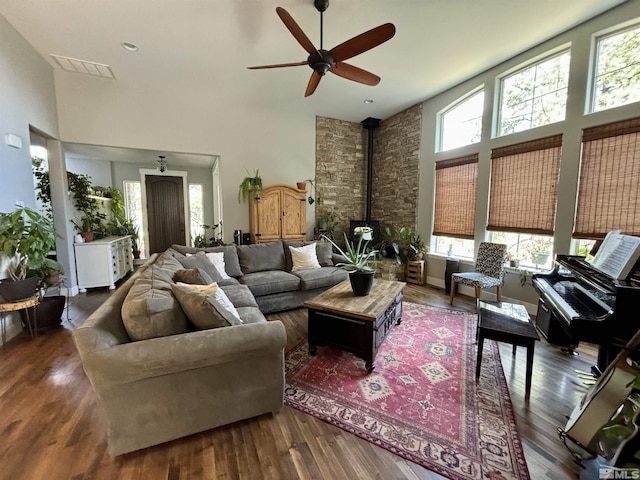 living room with a towering ceiling, dark wood-type flooring, ceiling fan, and a wood stove