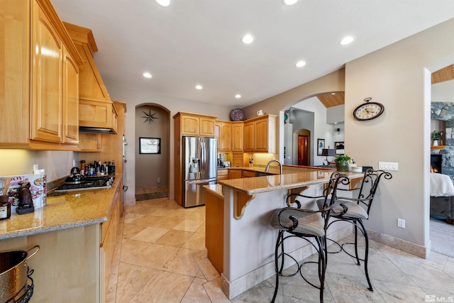 kitchen with a breakfast bar area, stainless steel fridge, black gas cooktop, light stone countertops, and kitchen peninsula