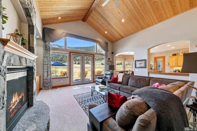 carpeted living room featuring beam ceiling, high vaulted ceiling, a fireplace, wooden ceiling, and french doors