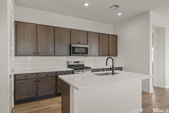 kitchen with appliances with stainless steel finishes, sink, decorative backsplash, dark brown cabinetry, and a center island with sink