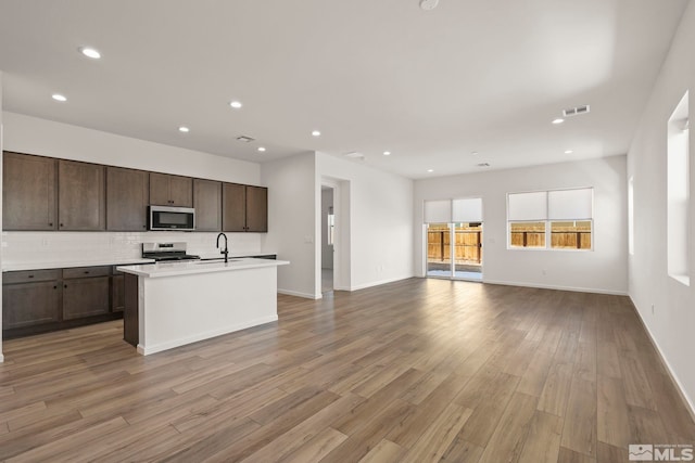 kitchen featuring tasteful backsplash, dark brown cabinetry, light hardwood / wood-style floors, stainless steel appliances, and a center island with sink