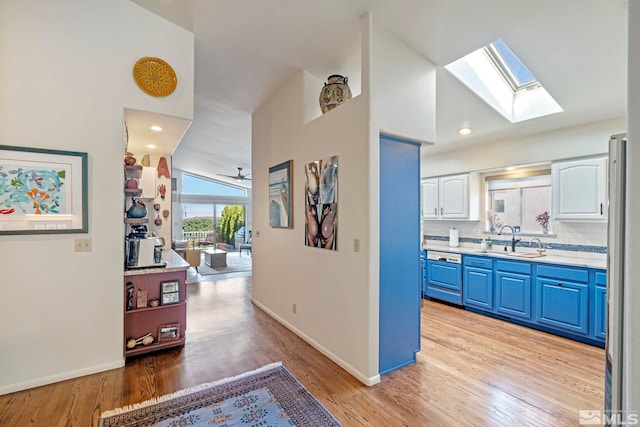 corridor featuring sink, vaulted ceiling with skylight, and light wood-type flooring