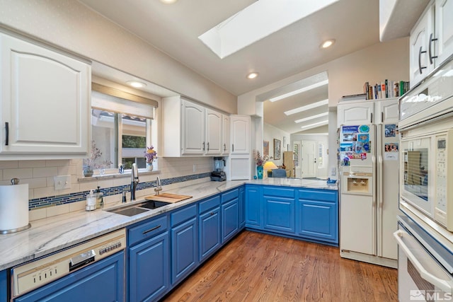 kitchen featuring dishwasher, white cabinets, white fridge with ice dispenser, stainless steel oven, and blue cabinetry