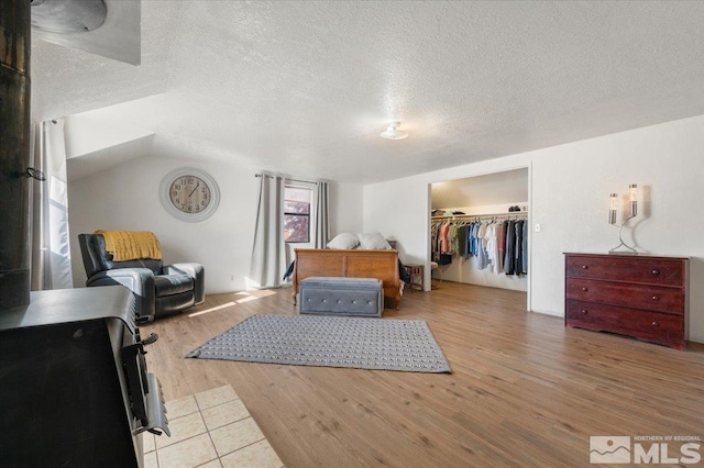 bedroom featuring a walk in closet, vaulted ceiling, light hardwood / wood-style flooring, a textured ceiling, and a closet