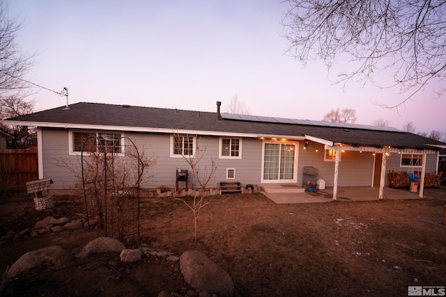 back house at dusk featuring a patio area and solar panels