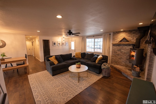 living room with dark wood-type flooring, ceiling fan, and a wood stove