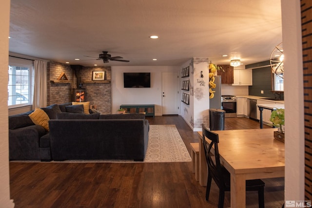 living room featuring sink, ceiling fan, dark hardwood / wood-style floors, brick wall, and a wood stove