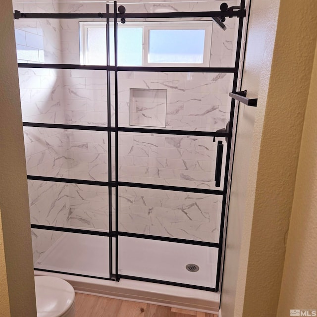 bathroom with hardwood / wood-style flooring, toilet, and a tile shower