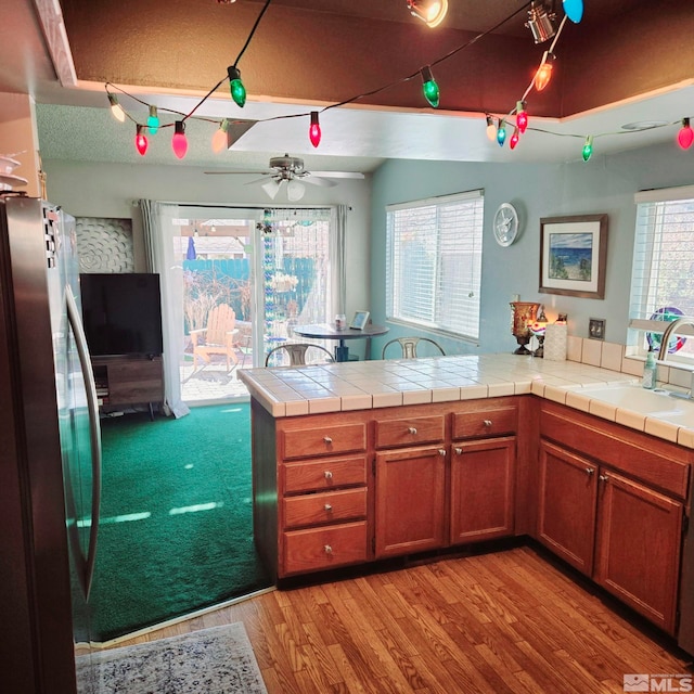 kitchen with sink, tile countertops, stainless steel fridge, and kitchen peninsula