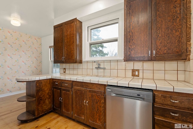 kitchen featuring sink, tile countertops, light hardwood / wood-style flooring, stainless steel dishwasher, and decorative backsplash