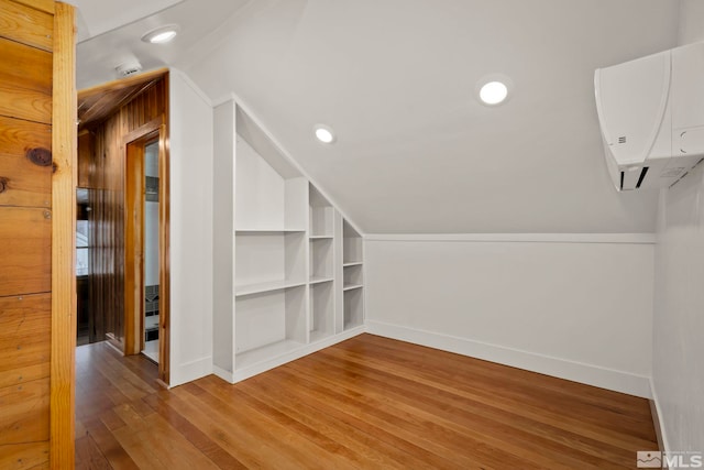 additional living space featuring built in features, lofted ceiling, wood-type flooring, and an AC wall unit