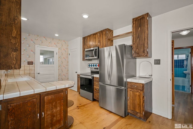 kitchen featuring appliances with stainless steel finishes, tile counters, sink, and light wood-type flooring