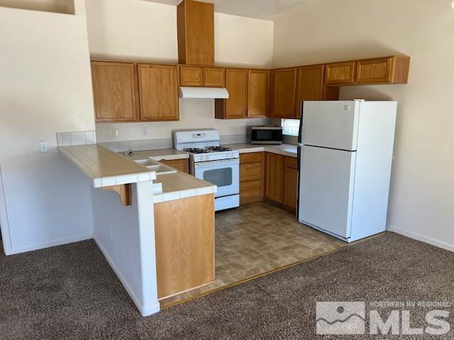 kitchen with a towering ceiling, carpet flooring, white appliances, and kitchen peninsula