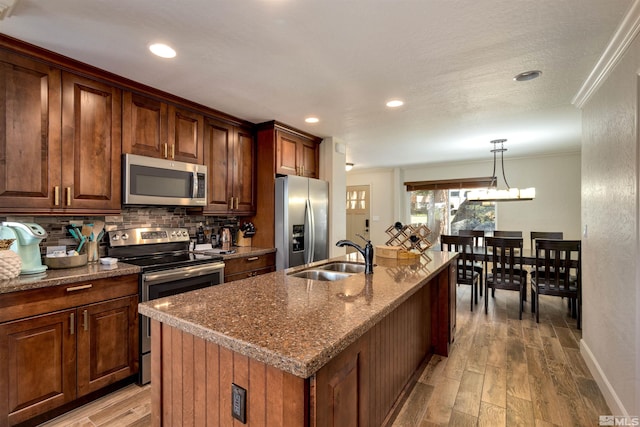 kitchen featuring decorative light fixtures, sink, stainless steel appliances, a center island with sink, and light wood-type flooring