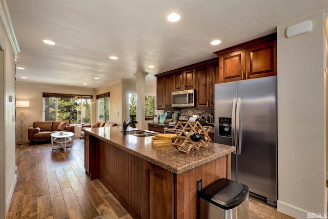 kitchen with crown molding, hardwood / wood-style flooring, stainless steel appliances, and a center island with sink