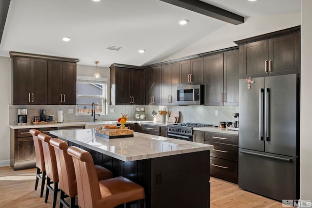 kitchen featuring pendant lighting, appliances with stainless steel finishes, vaulted ceiling with beams, dark brown cabinetry, and a kitchen island