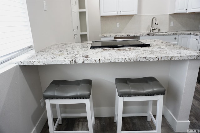 kitchen with sink, white cabinetry, stove, a kitchen breakfast bar, and decorative backsplash