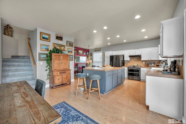 kitchen with a kitchen bar, white cabinetry, a kitchen island, stainless steel appliances, and light hardwood / wood-style floors