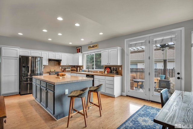 kitchen with a kitchen island, white cabinetry, dishwashing machine, stainless steel fridge, and light hardwood / wood-style flooring