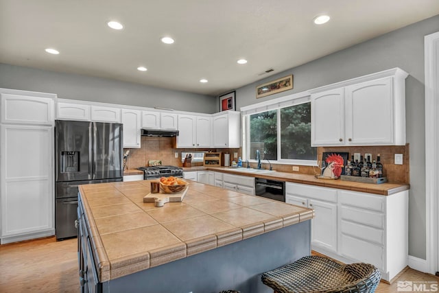 kitchen with sink, appliances with stainless steel finishes, white cabinetry, backsplash, and tile counters