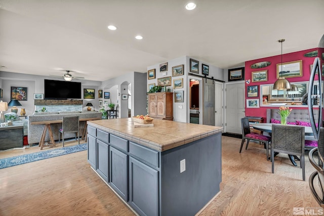 kitchen featuring tile countertops, pendant lighting, ceiling fan, light hardwood / wood-style floors, and a barn door