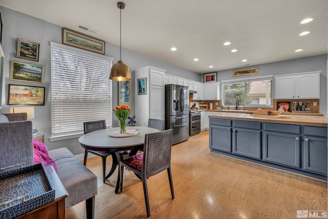 kitchen with sink, decorative light fixtures, appliances with stainless steel finishes, light hardwood / wood-style floors, and white cabinets