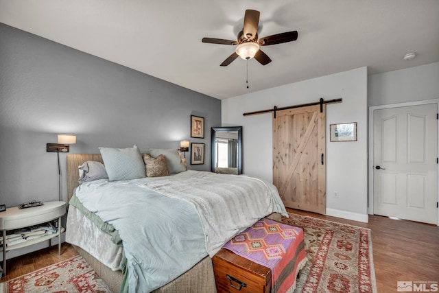 bedroom with ceiling fan, a barn door, and dark hardwood / wood-style flooring