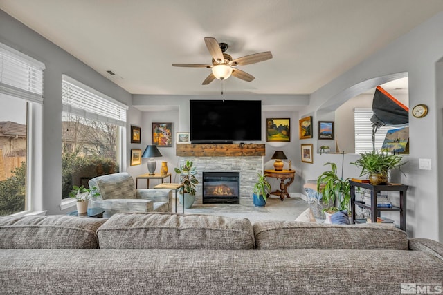 living room featuring ceiling fan, a stone fireplace, and carpet