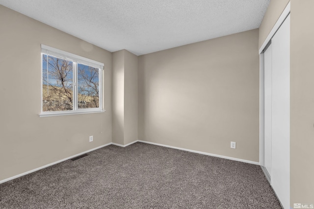 unfurnished bedroom featuring dark colored carpet, a textured ceiling, and a closet