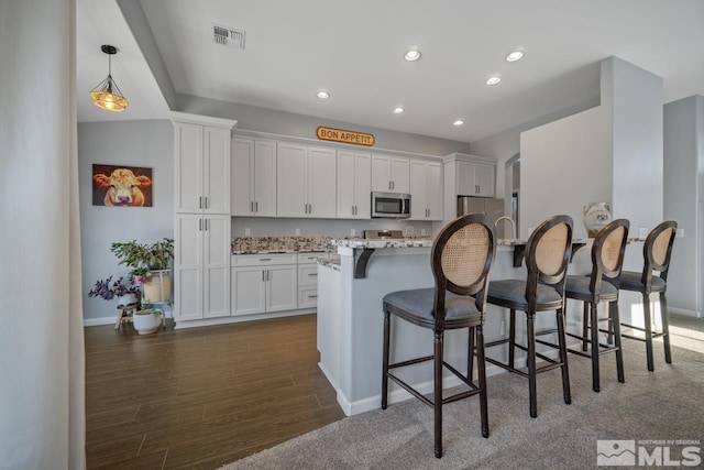 kitchen featuring a kitchen bar, white cabinetry, decorative light fixtures, dark hardwood / wood-style floors, and stainless steel appliances