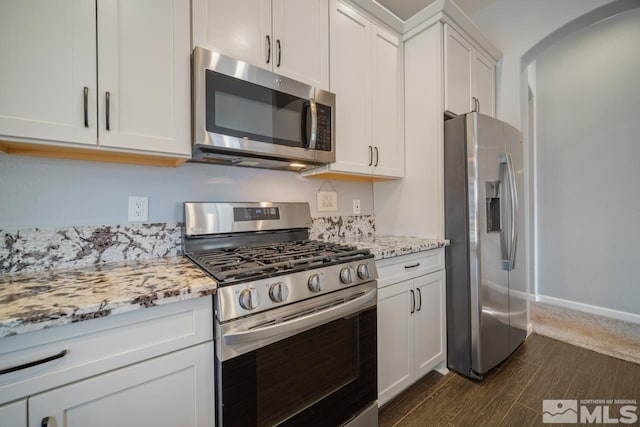 kitchen with dark wood-type flooring, light stone countertops, white cabinets, and appliances with stainless steel finishes