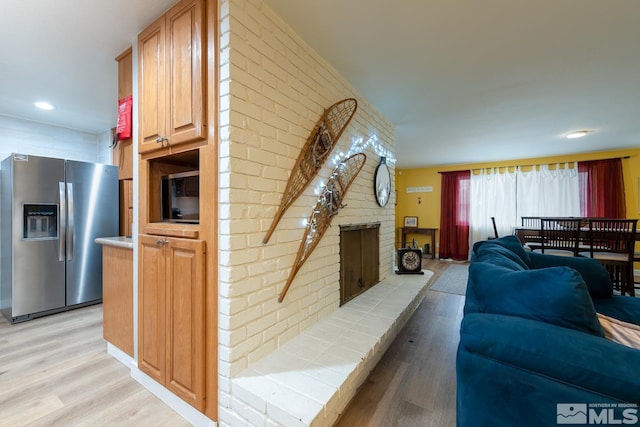 living room with brick wall, a brick fireplace, and light hardwood / wood-style flooring