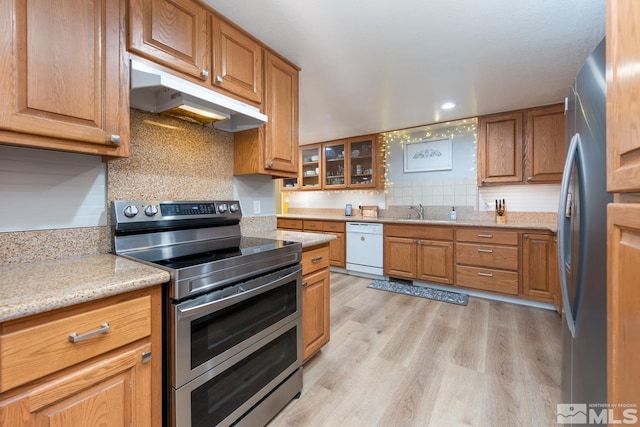 kitchen with sink, appliances with stainless steel finishes, light stone countertops, decorative backsplash, and light wood-type flooring