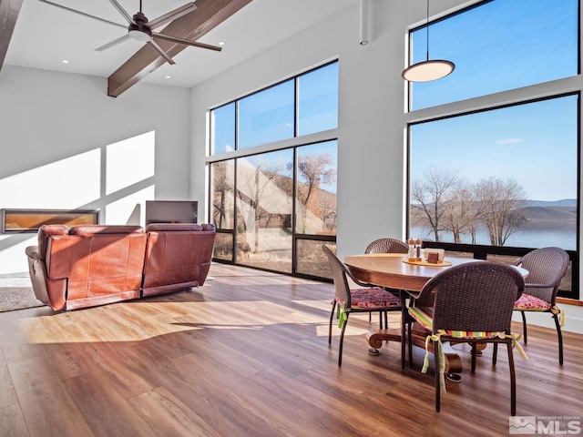 dining space featuring beam ceiling, wood-type flooring, ceiling fan, and a high ceiling