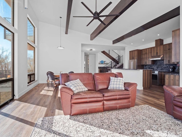 living room featuring dark hardwood / wood-style flooring, ceiling fan, a towering ceiling, and beamed ceiling