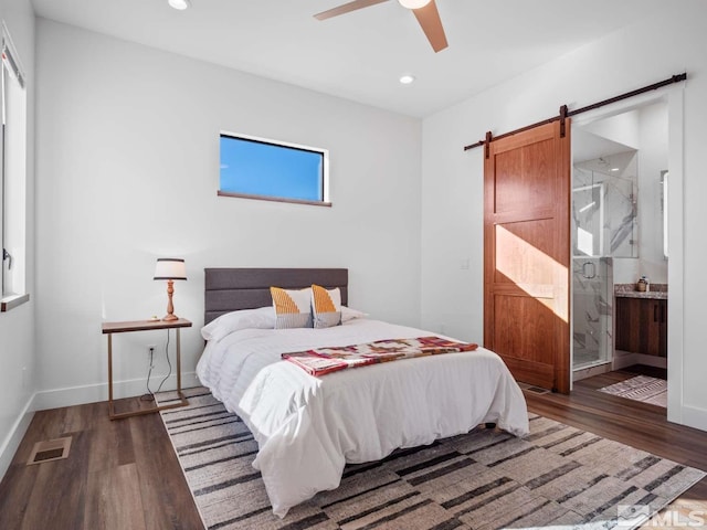 bedroom featuring a barn door, dark hardwood / wood-style floors, connected bathroom, and ceiling fan