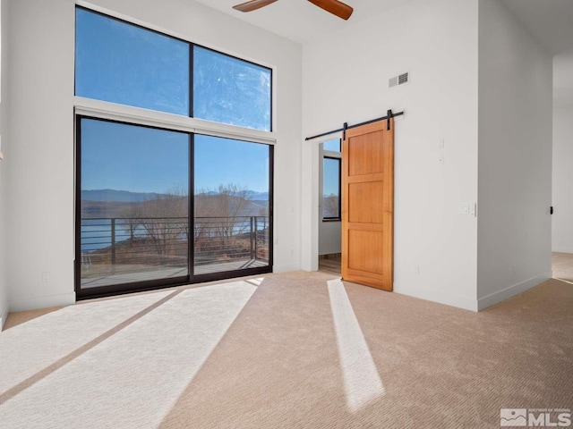 unfurnished bedroom with a towering ceiling, carpet floors, access to exterior, ceiling fan, and a barn door