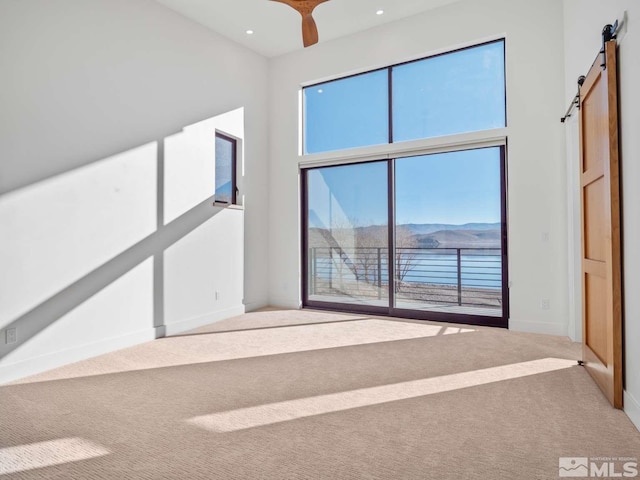 unfurnished living room featuring a mountain view, a towering ceiling, carpet floors, and a barn door