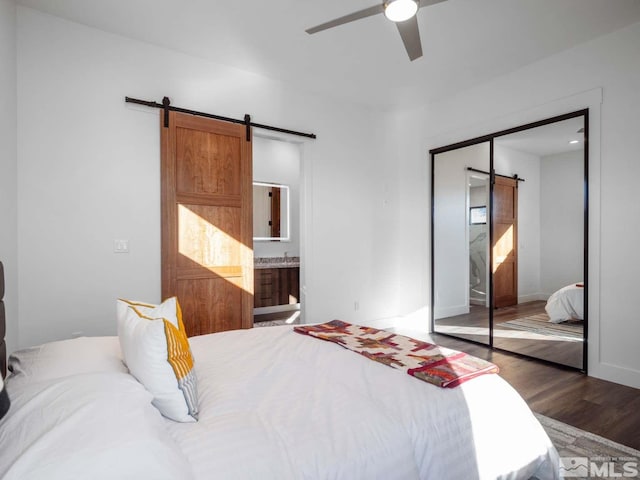 bedroom with ceiling fan, connected bathroom, a barn door, dark hardwood / wood-style flooring, and a closet