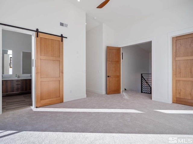 unfurnished bedroom featuring high vaulted ceiling, light colored carpet, ceiling fan, a barn door, and ensuite bath