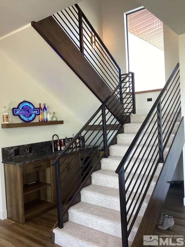 stairs with hardwood / wood-style flooring and bar area