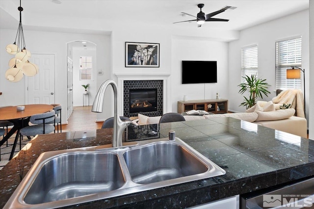 kitchen with a tile fireplace, hardwood / wood-style floors, decorative light fixtures, sink, and ceiling fan