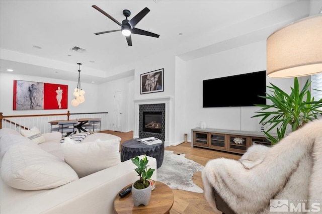 living room featuring a tiled fireplace, ceiling fan, and light wood-type flooring