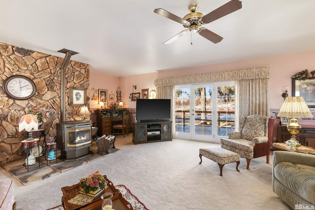 carpeted living room with ceiling fan and a wood stove