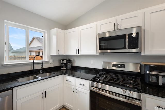 kitchen featuring appliances with stainless steel finishes, white cabinetry, lofted ceiling, sink, and dark stone countertops